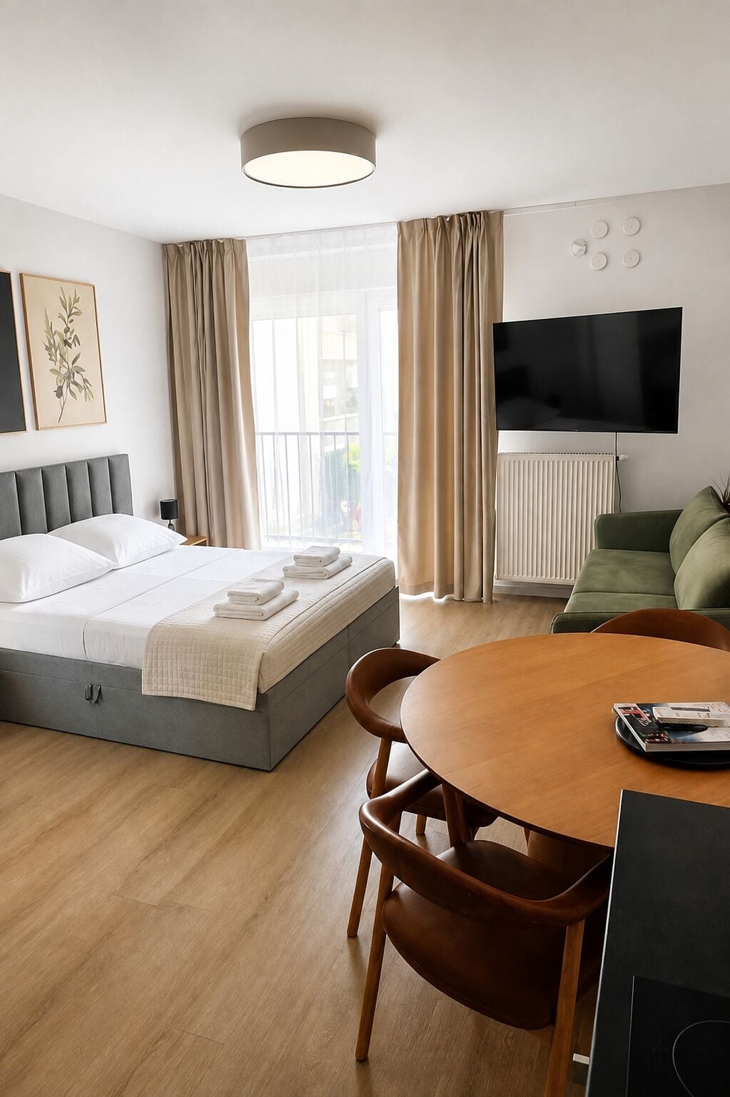 Une chambre d’hôtel avec un lit, une télévision, une table à manger et une fenêtre avec des rideaux.