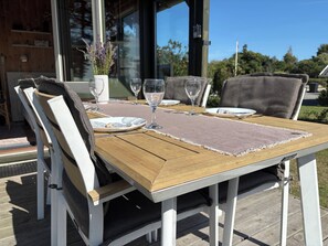 Une table à manger extérieure, avec des chaises, des sets de table et des verres à vin.