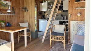 A wooden interior with a dining area, kitchen, and a loft bedroom. - Cozy small holiday home with sea view (Sydals)