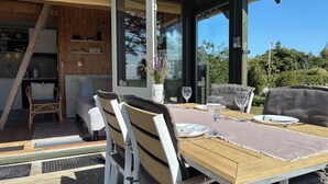 An outdoor dining area with a wooden table, white chairs, and a glass window. - Cozy small holiday home with sea view (Sydals)