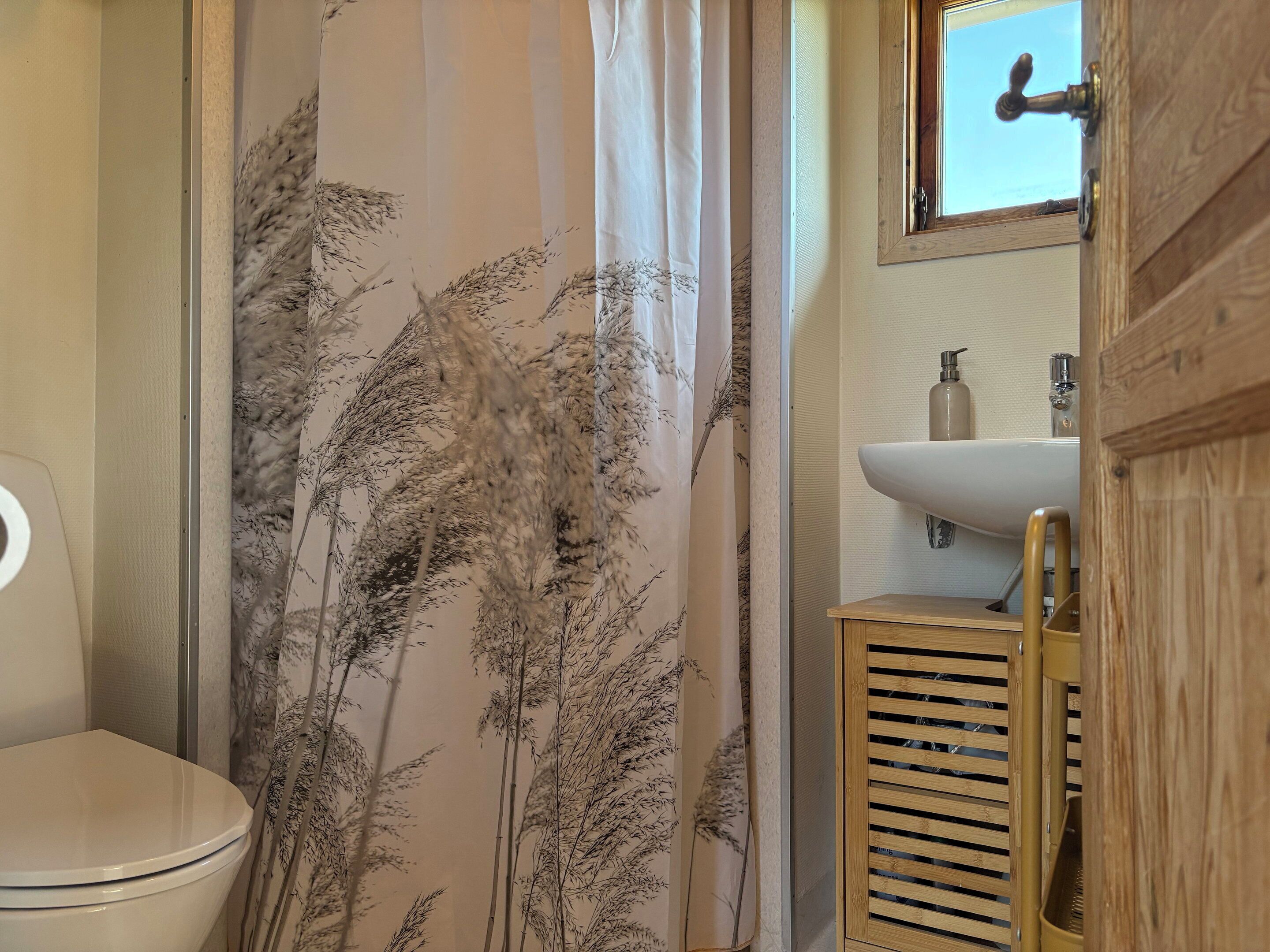 Une salle de bain équipée de toilettes, d’un lavabo et d’un rideau de douche à motifs floraux.