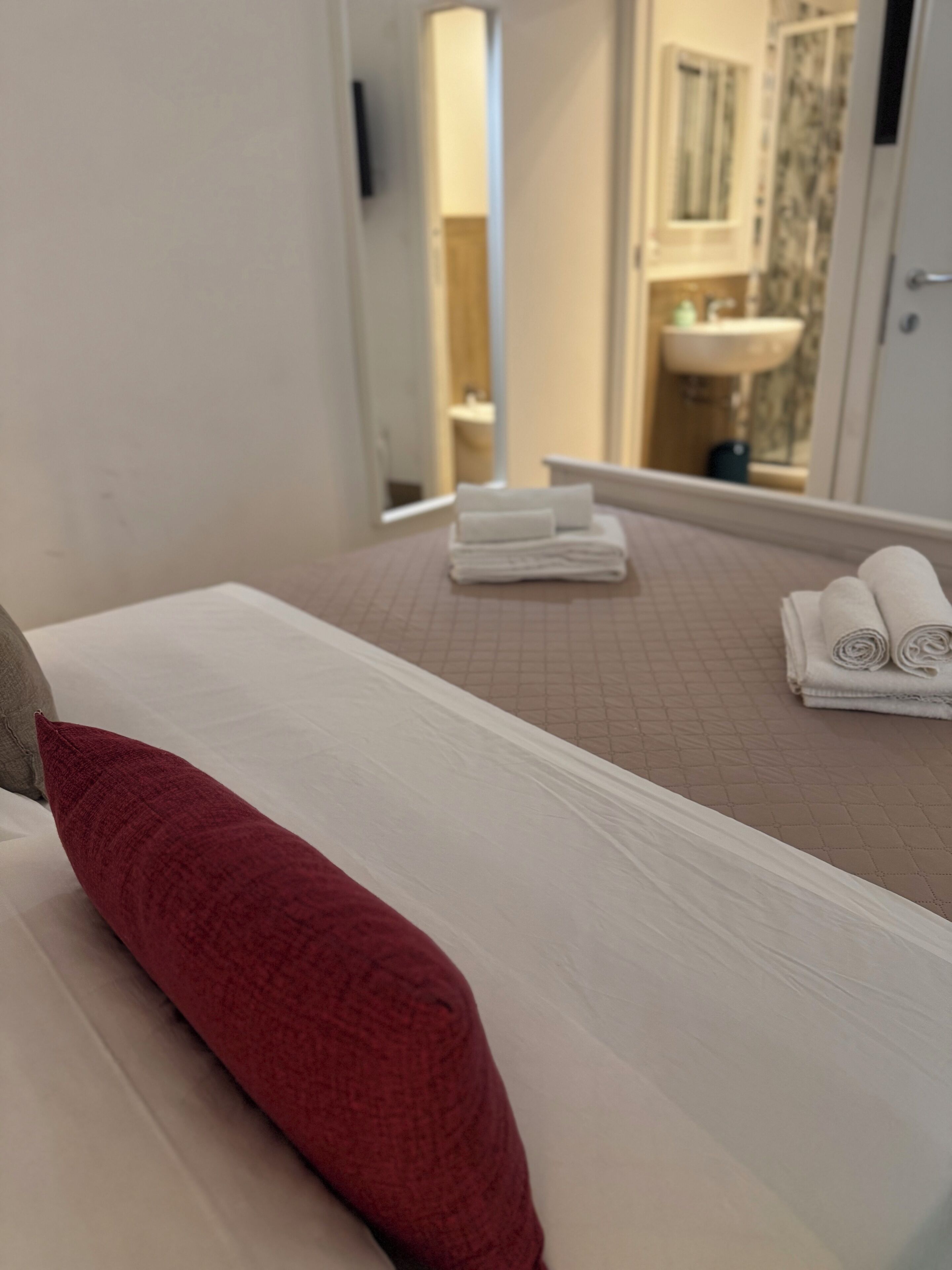 Une chambre d’hôtel avec un lit, un oreiller rouge et des serviettes soigneusement pliées sur la table de chevet.
