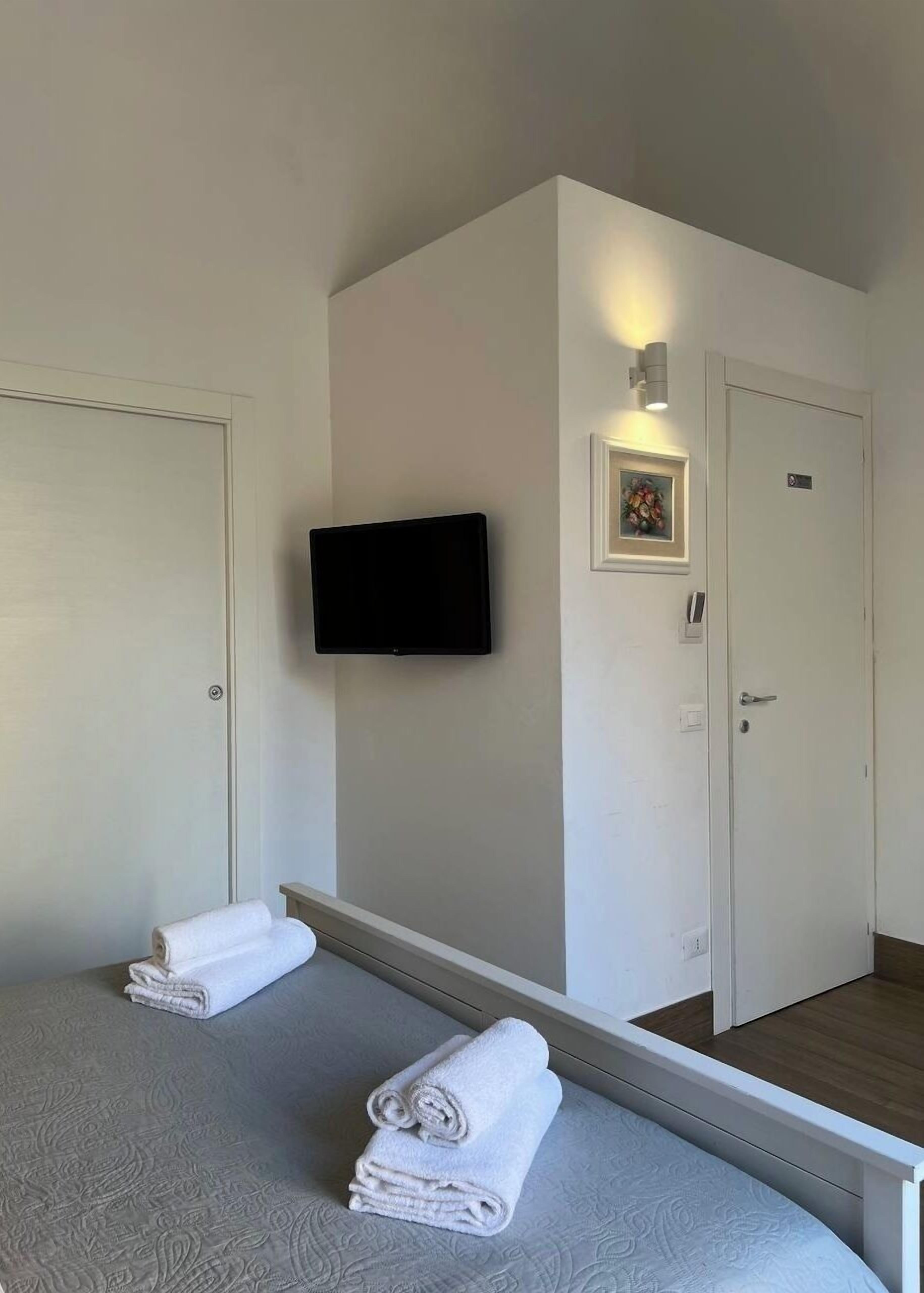 Une chambre d’hôtel avec un lit, un téléviseur fixé au mur, une porte et un tableau encadré.