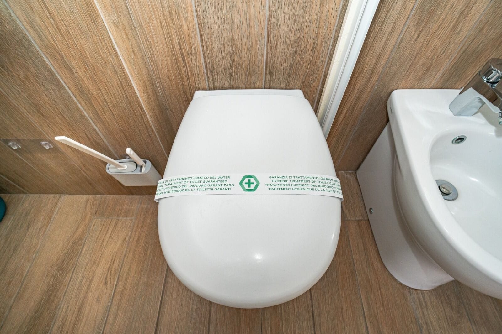 Un baño moderno con inodoro y lavamanos blancos, paneles de madera y un cartel de garantía de higiene.