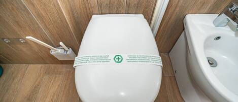 Un baño moderno con inodoro y lavamanos blancos, paneles de madera y un cartel de garantía de higiene.