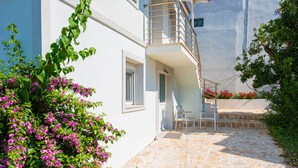 En hvid bygning med en brostensbelagt gårdsplads, en balkon med gelænder og en stol udenfor.