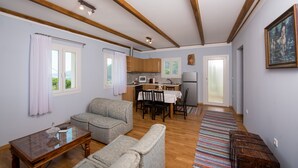 A living room with a sofa, a coffee table, a kitchen area with a microwave, and a dining table with chairs. - Holiday Home 'Lovely' with Balcony, Wi-Fi and Air Conditioning (Sivros)