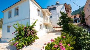 A two-story building with a balcony, a staircase, and a garden with pink flowers. - Holiday Home 'Lovely' with Balcony, Wi-Fi and Air Conditioning (Sivros)