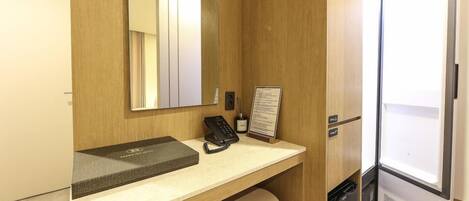 Un baño de hotel con tocador de madera, un espejo, un teléfono y un cubo de basura.