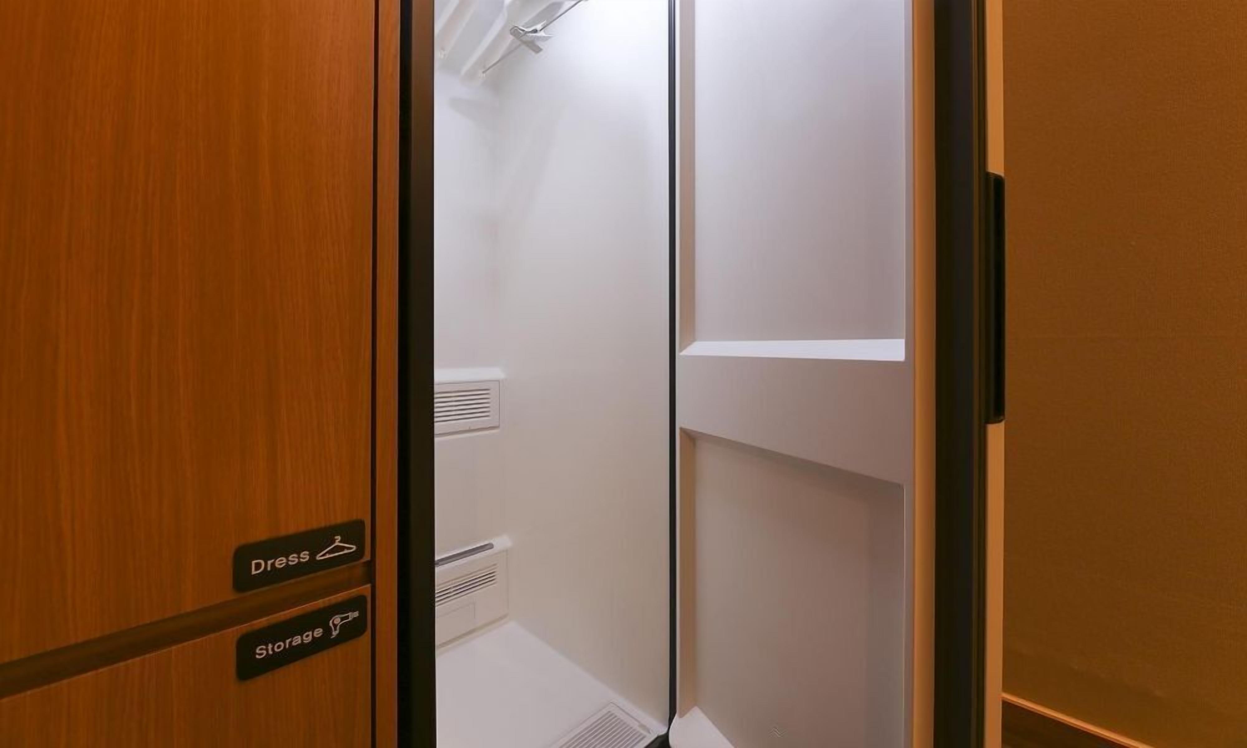 A hotel room with a wooden door, a white wall, and a small shelf.