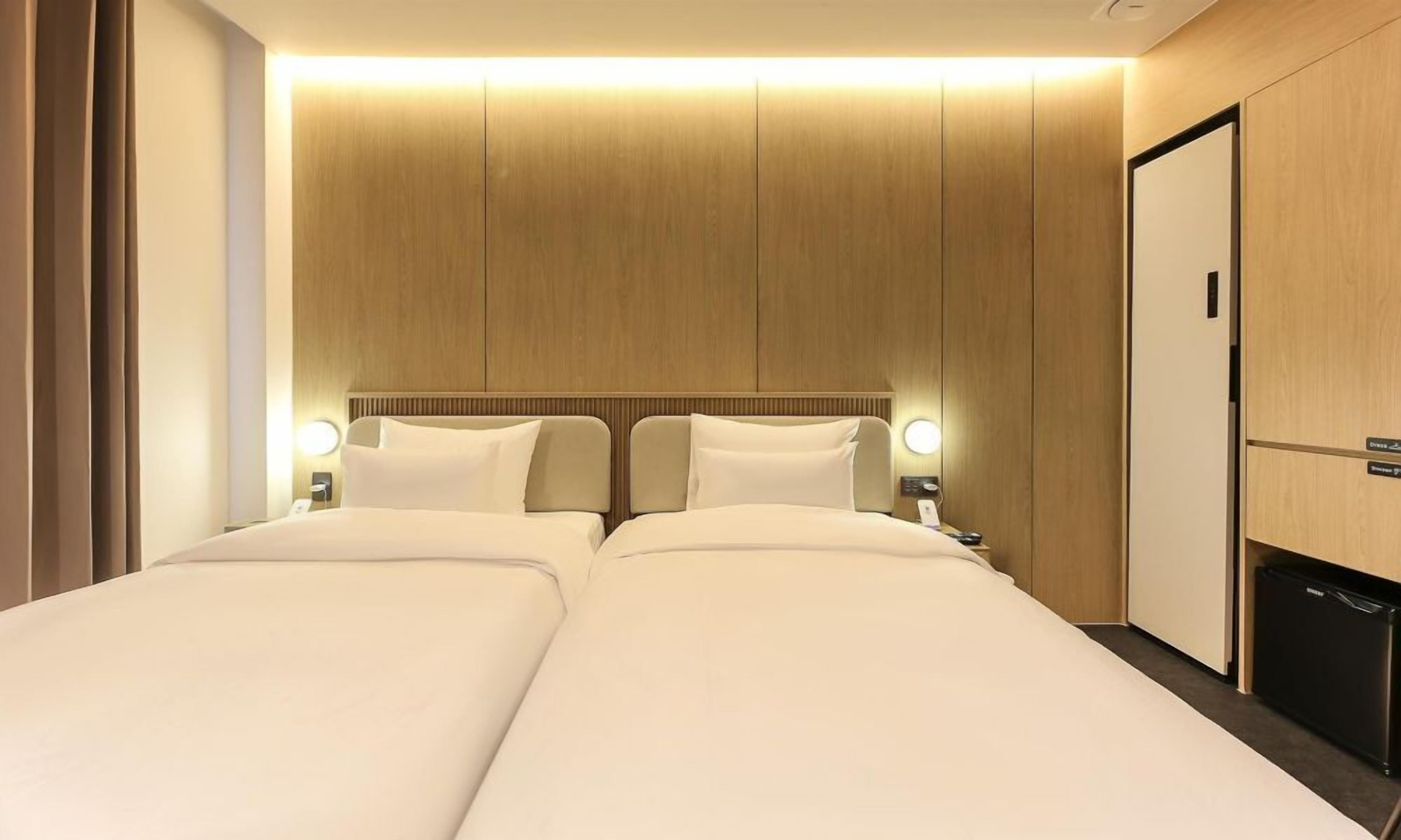 Habitación de hotel con dos camas, cabecero de madera, lámparas de noche y minibar.