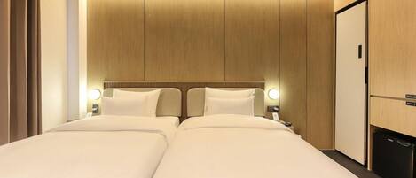 Habitación de hotel con dos camas, cabecero de madera, lámparas de noche y minibar.