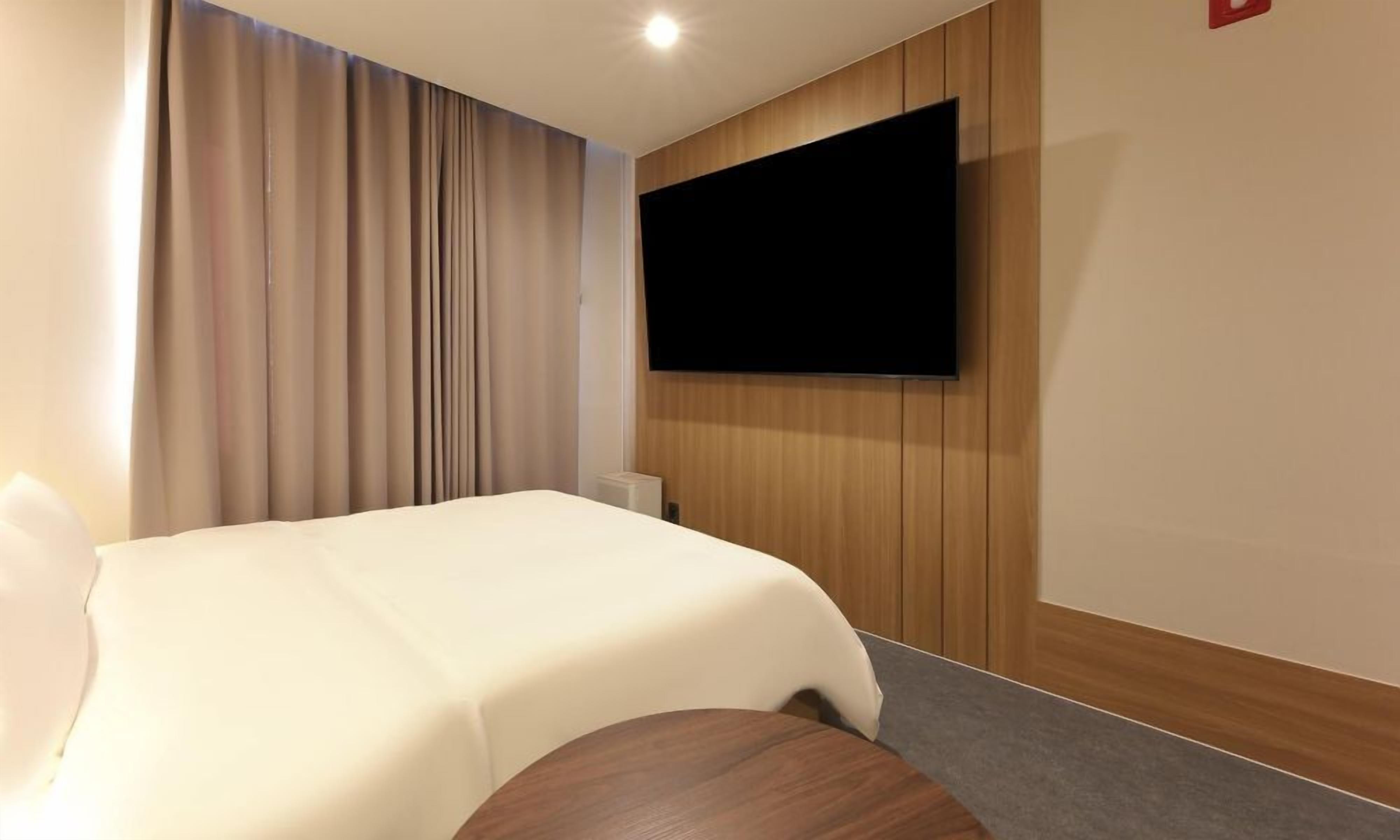 Une chambre d’hôtel avec un lit, un téléviseur fixé au mur et une fenêtre avec des rideaux.