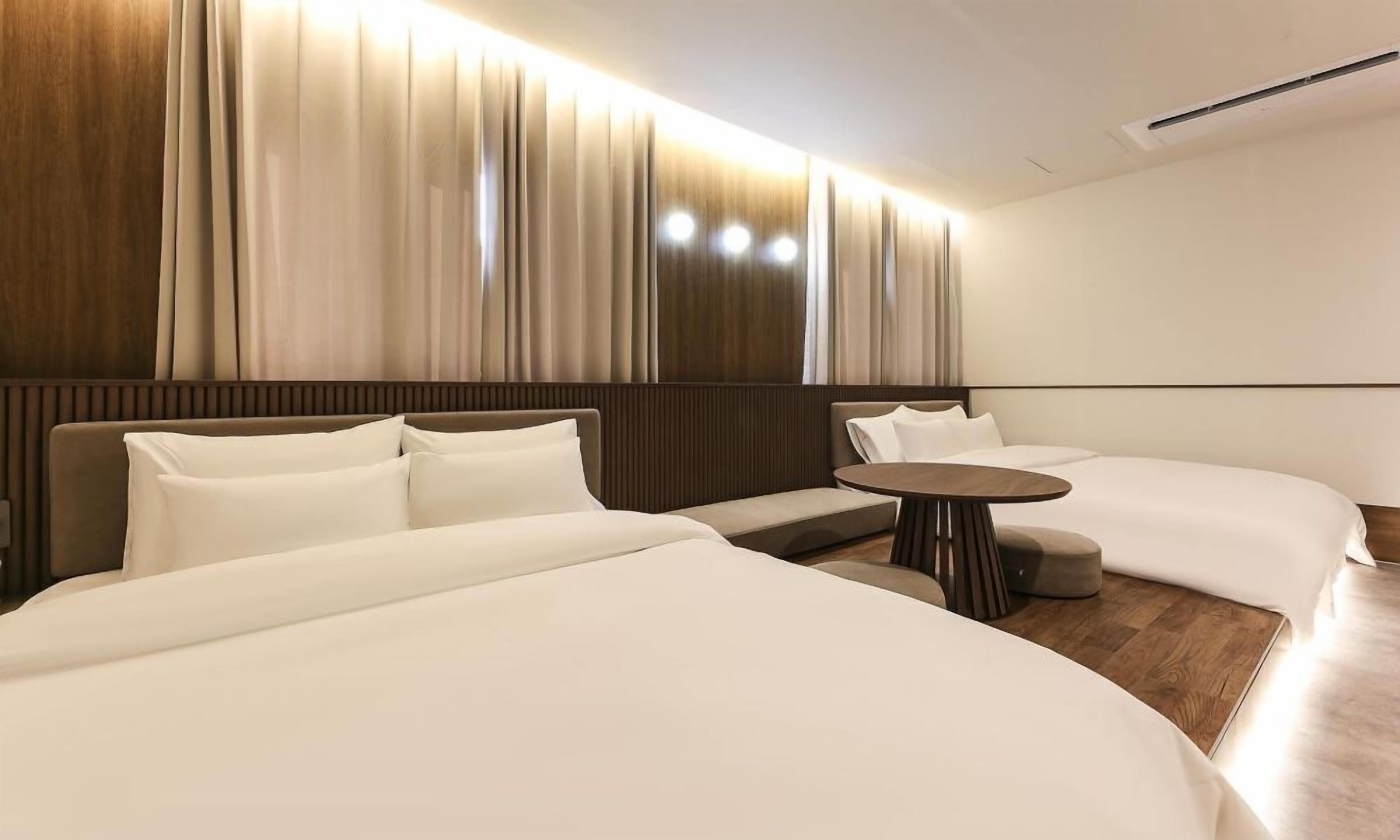 A modern hotel room with a large bed, a smaller bed, a sofa, and a round table.