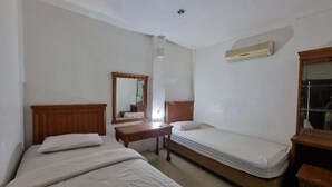 A room with two beds, a wooden nightstand, a mirror, and a wall-mounted heater.