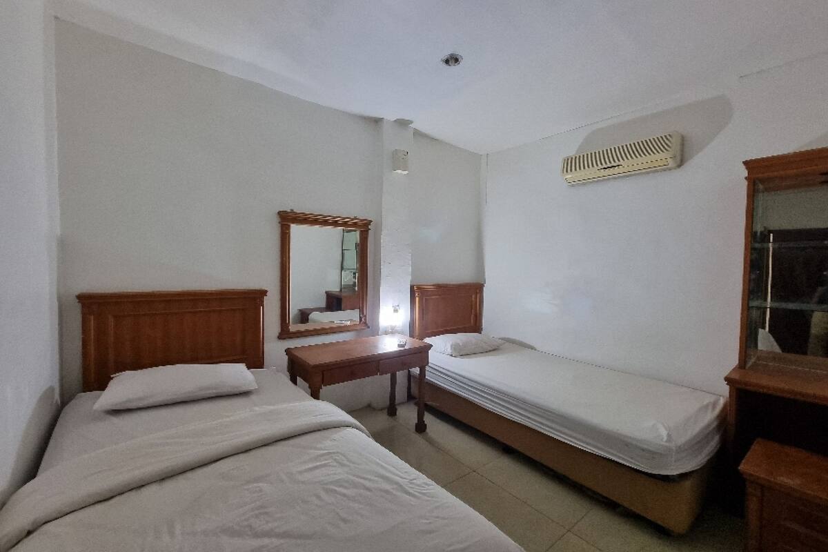 Una habitación con dos camas, una mesita de noche de madera, un espejo y un calentador fijado a la pared.