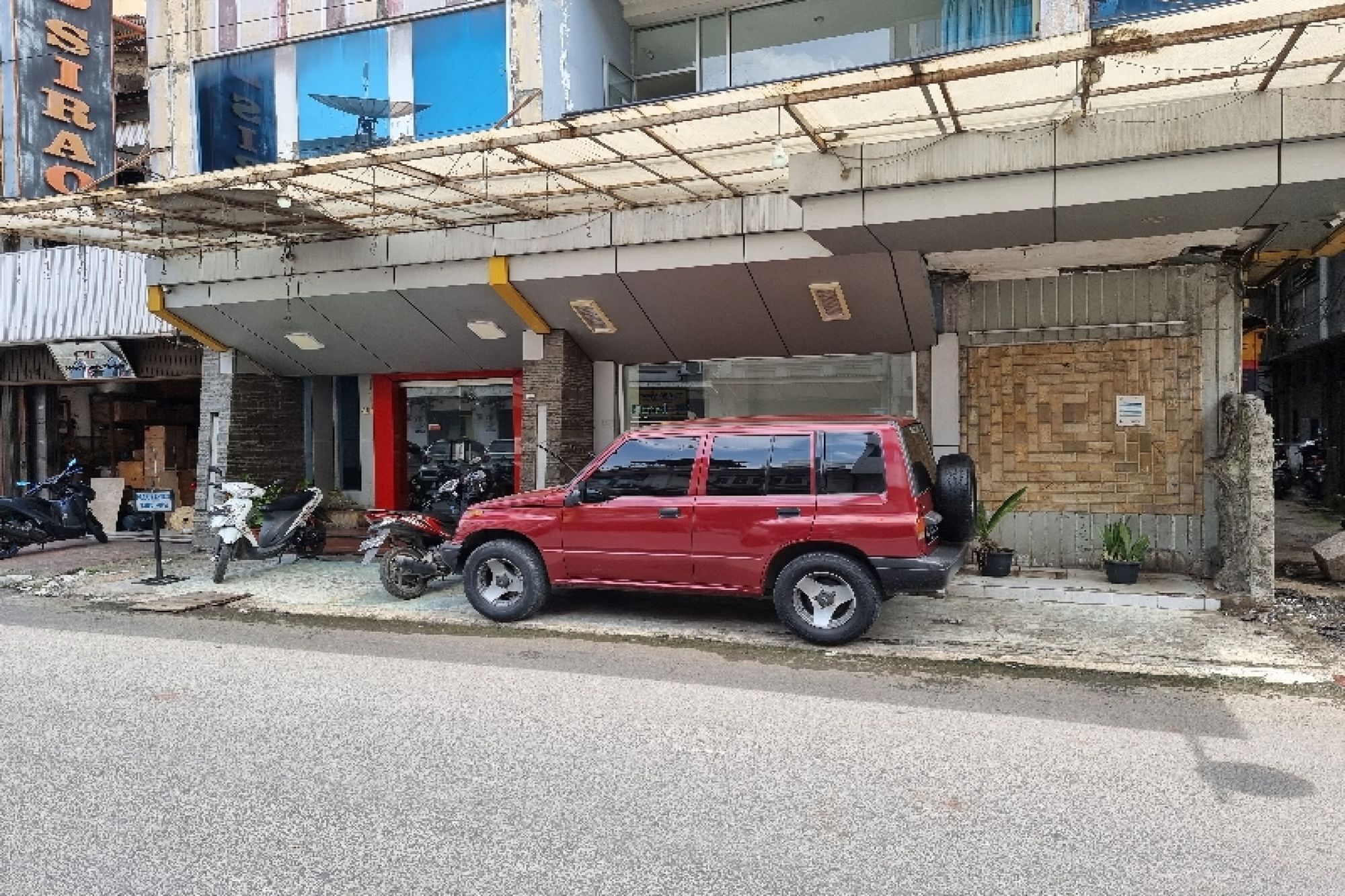 Um SUV vermelho estacionado em frente a um edifício com entrada coberta e uma placa.