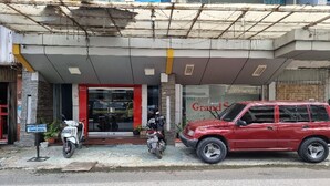 A hotel entrance with a red car parked outside, a motorcycle, and a signboard.