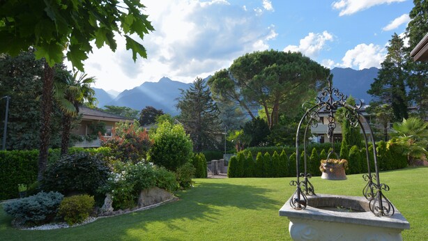 Ein gepflegter Garten mit Springbrunnen, geschnittenen Rasenflächen und einer Bergkulisse im Hintergrund.