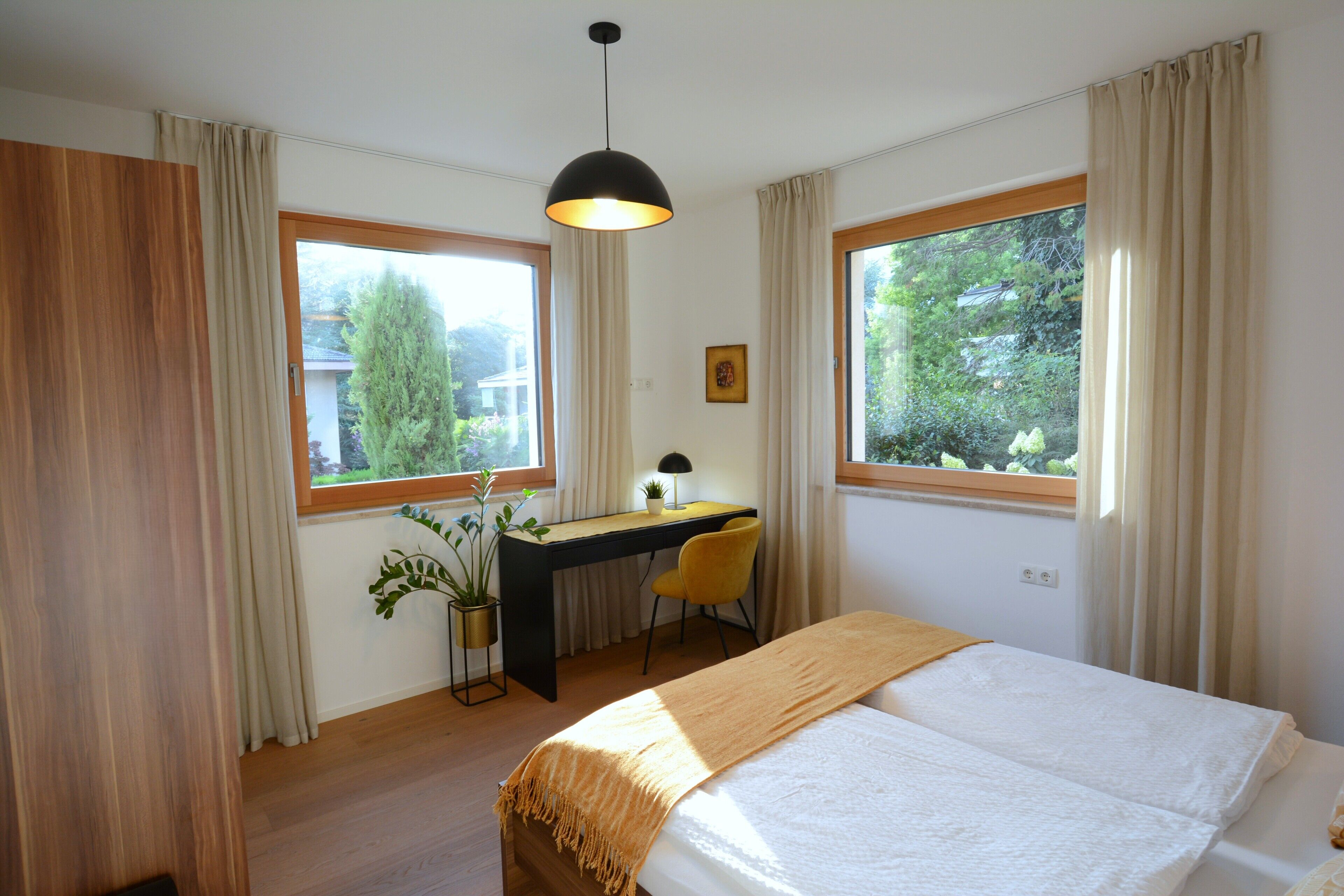 Een slaapkamer met een bed, bureau, stoel en grote ramen.