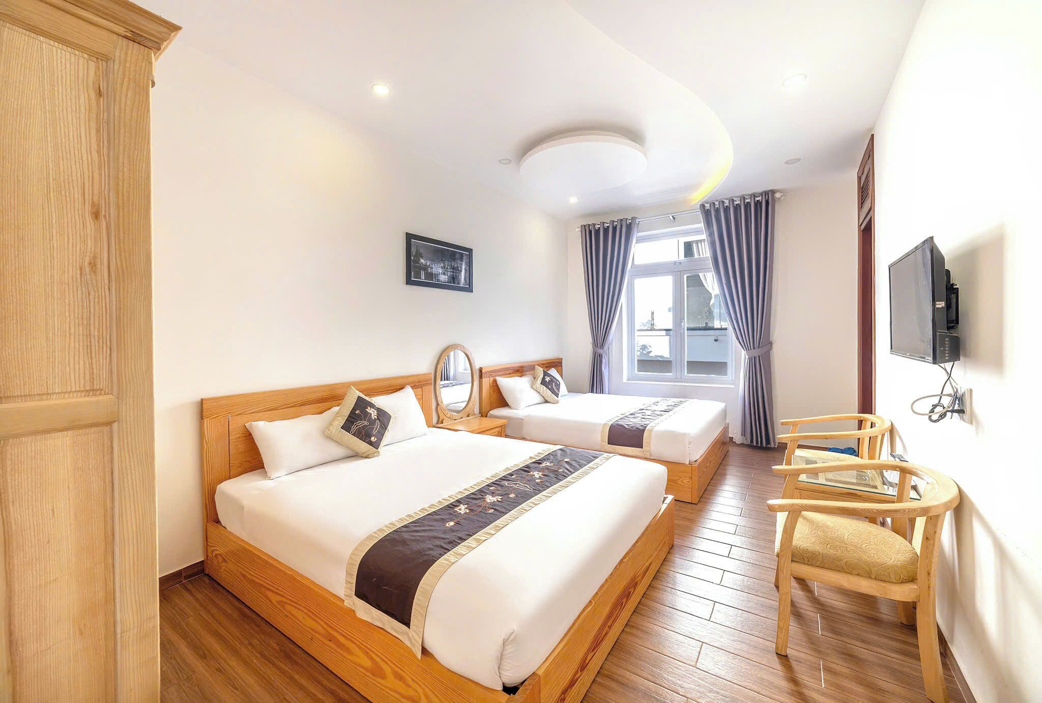 A hotel room with two wooden beds, a wooden wardrobe, a TV, and a desk with a chair.