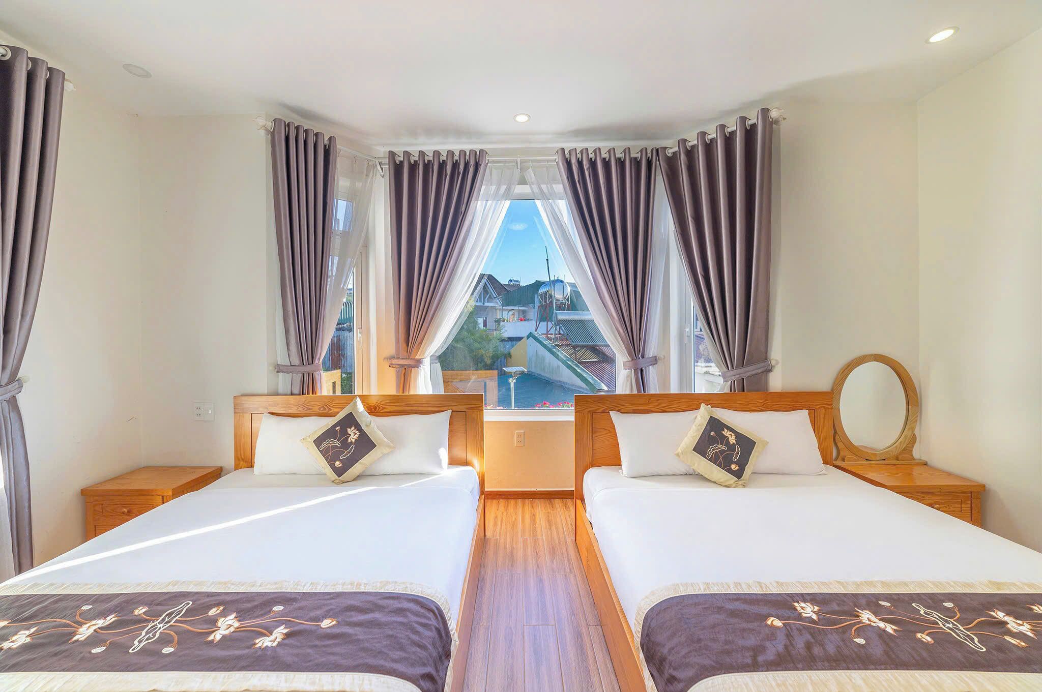 A hotel room with two beds, a wooden headboard, a small table, and a view of a cityscape through the window.