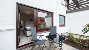 An outdoor patio with a table and chairs, a sliding glass door leading to a room, and a small garden area with plants.
