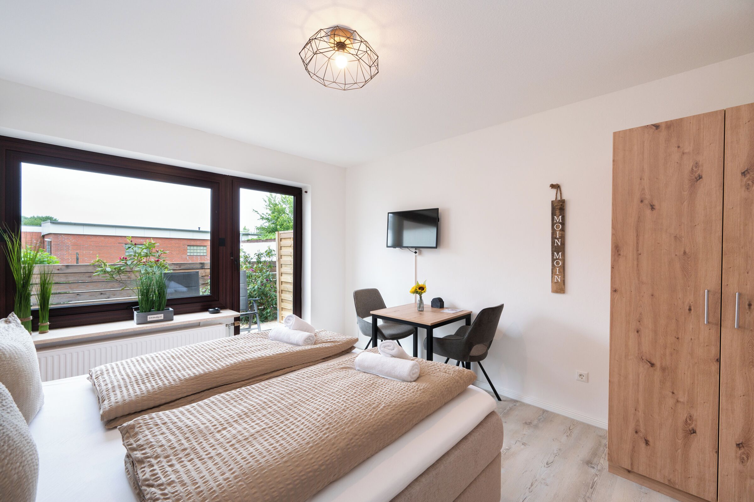Ein Schlafzimmer mit großem Fenster, einem Bett, einem Schreibtisch mit Stühlen und einem Kleiderschrank.