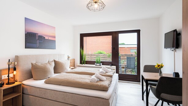 A bedroom with a large bed, bedside tables, a TV, and a window with a view of the outside.