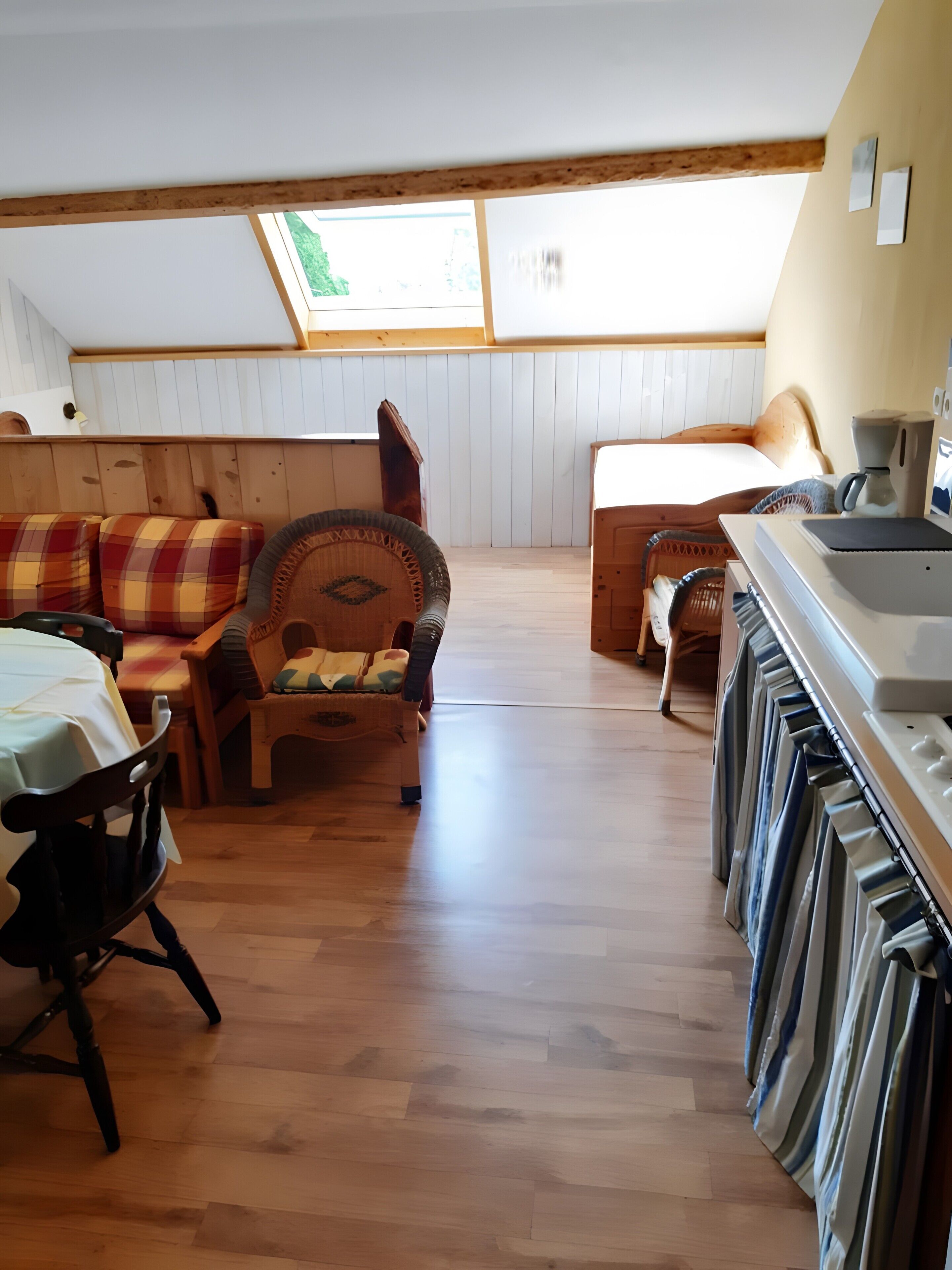 A cozy room with a wooden floor, a sofa, a chair, a bed, and a kitchenette.