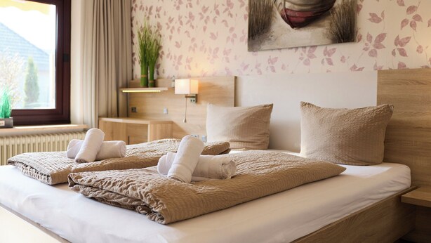 A hotel room with a large bed, a headboard, a nightstand, a lamp, a painting, and a window with curtains.