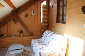 A cozy attic room with wooden walls, a patterned sofa, a small table, and a window with curtains.