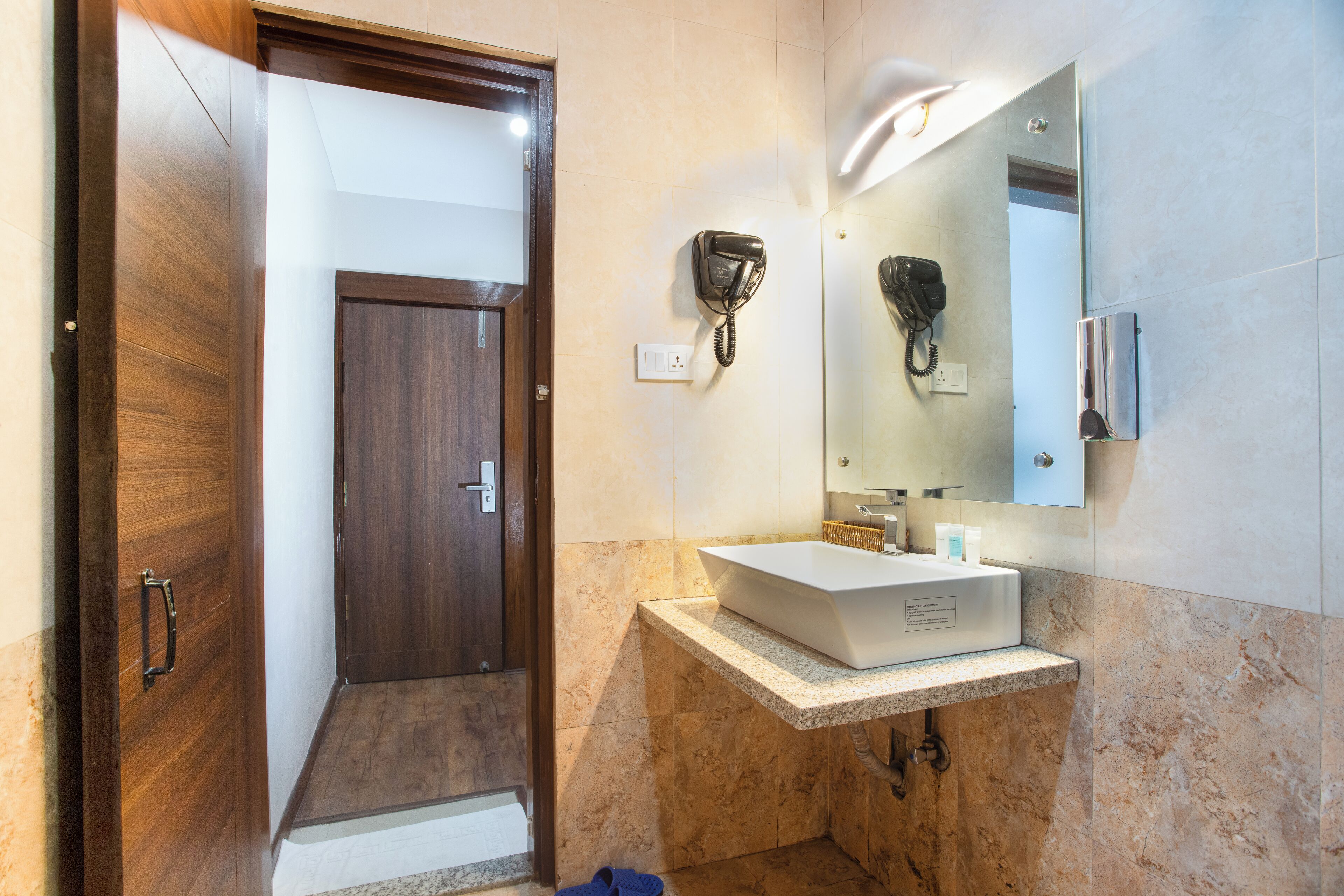 Un baño con puerta de madera, un lavabo blanco, un secador de pelo y un espejo.