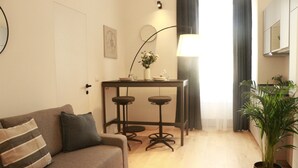 A living room with a sofa, a small table with stools, a lamp, and a potted plant.