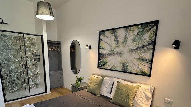 A modern bedroom with a large bed, a wardrobe, a mirror, and a painting on the wall.