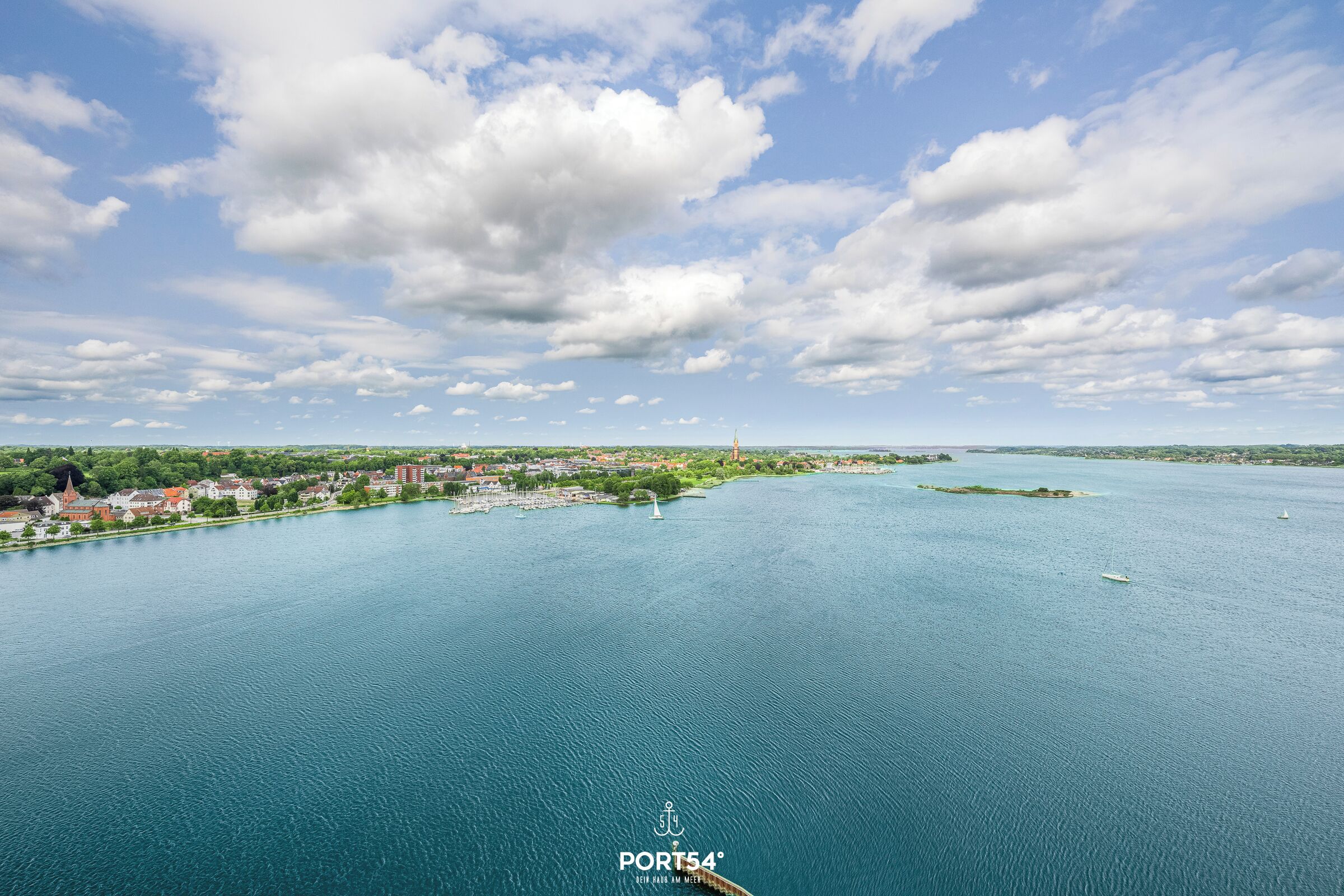 An aerial view of a coastal town with a large body of water, a lighthouse, and a bridge.