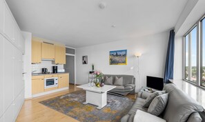 A modern living room with a sofa and a coffee table, a kitchen with cabinets and appliances, and a large window with a view. - Wikingturm 20.4 - 20th Floor, 1 Room, View of the Schlei, Underground Parking (Schleswig)