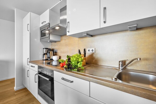 A modern kitchen with white cabinetry, a stainless steel sink, and a built-in oven. - Enjoy - Parking space, balcony, grill, washing machine, first row on the water (Olpenitz)