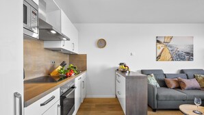 A modern kitchen with stainless steel appliances, a wooden countertop, and a grey sofa in the living area.