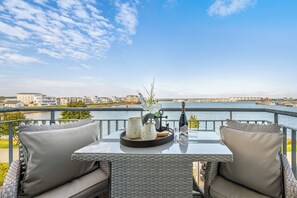 A balcony with a table set for two, overlooking a marina and buildings. - Enjoy - Parking space, balcony, grill, washing machine, first row on the water (Olpenitz)