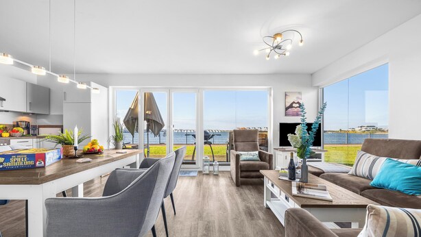 Una sala de estar moderna con comedor, ventanas grandes y vista al mar.