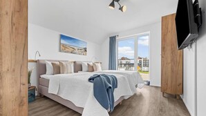 A bedroom with a bed, a TV, a window, and a painting.
