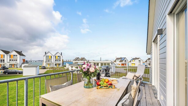 A balcony with a table set for dining, a vase of flowers, and a fruit basket.