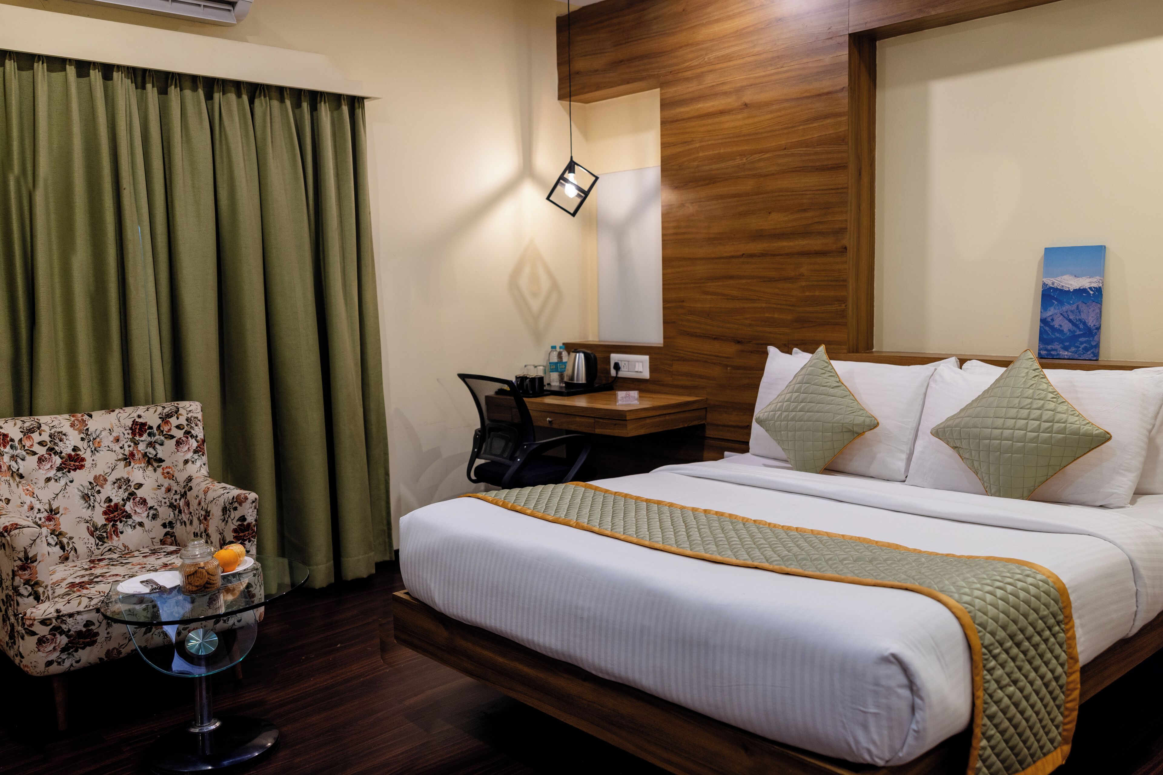 A hotel room with a large bed, a floral armchair, a small table with a glass top, and a wooden headboard.