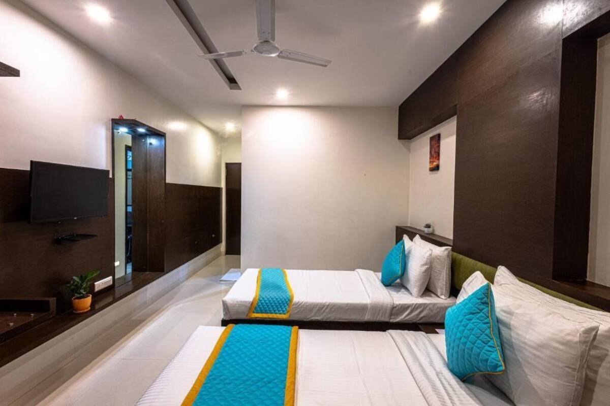 A hotel room with two beds, a ceiling fan, a flat-screen TV, and a small potted plant.