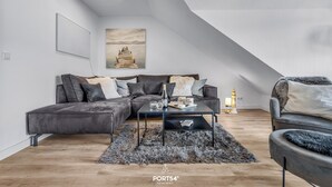A modern living room with a sectional sofa, a coffee table, and a painting on the wall. - Ferienwohnung Küstentiet - 2 balconies, 2 TVs, rural setting,by the sea, parking (Brodersby-Schönhagen)