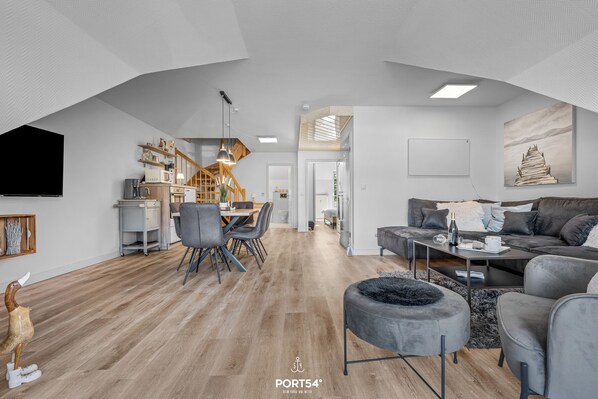 A modern living room with a dining area, a staircase, and a kitchen.