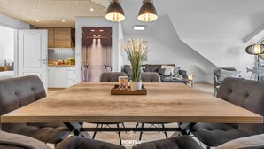 A modern dining area with a wooden table, black upholstered chairs, and pendant lighting. - Ferienwohnung Küstentiet - 2 balconies, 2 TVs, rural setting,by the sea, parking (Brodersby-Schönhagen)