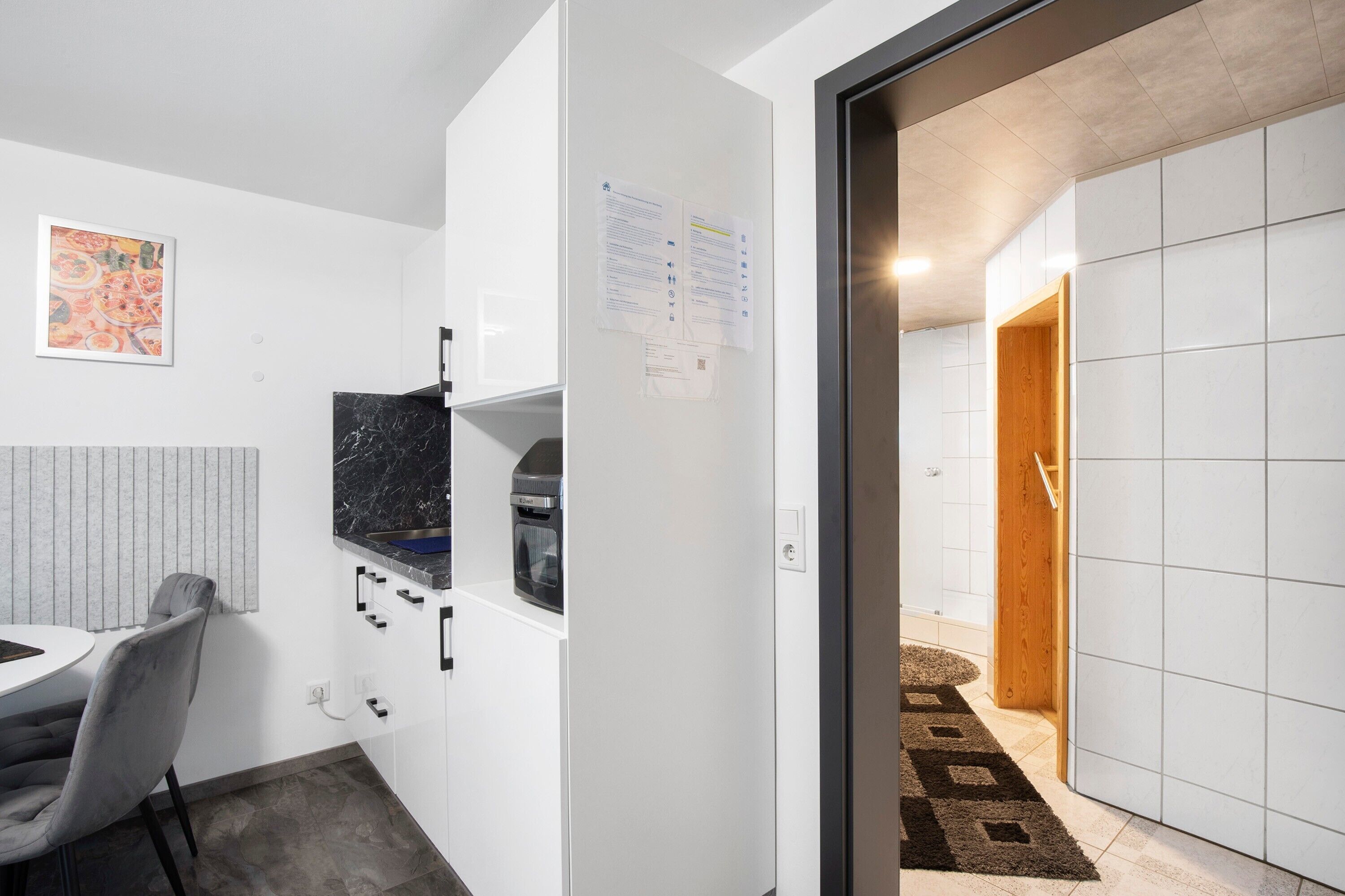 A modern kitchen with a marble countertop, a built-in oven, and a dining area with a chair and table.