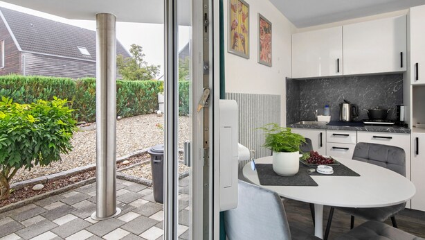 A modern kitchen with white cabinets, a marble countertop, and a dining area with a table and chairs.